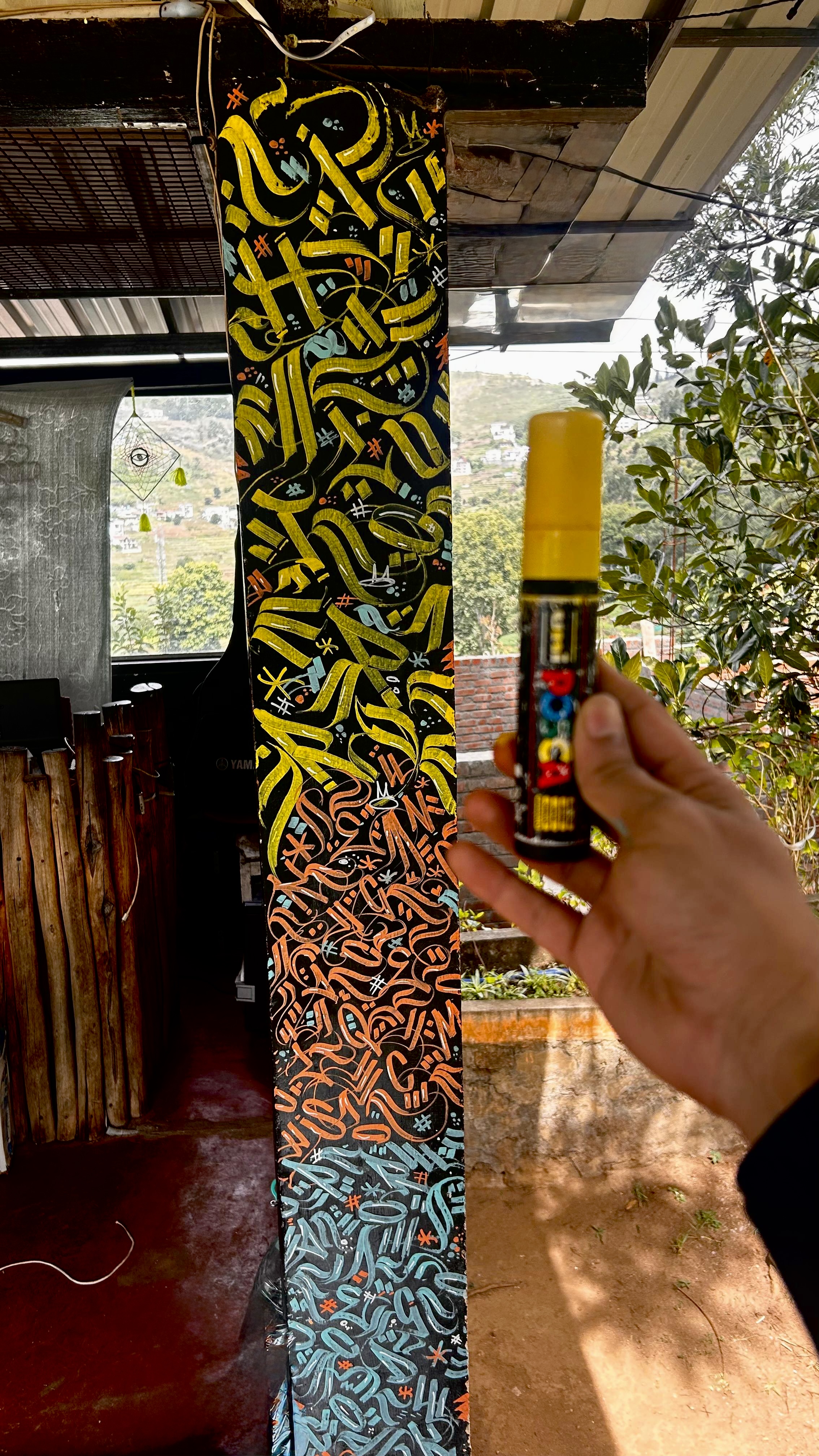 A paint marker held in front of a colourful graffiti-covered pillar
